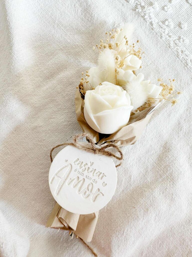 Ramo de flores de cera beije e branco com borboleta para oferecer. com medalha em gesso perfumado com a mensagem "ensinar é um ato de amor"