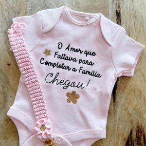 Body Personalizado para bebé ou criança com flores douradas e mensagem "o amor que faltava para completar a familia chegou!" e porta chupetas em crochê rosa com flor