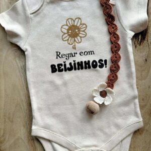 Body personalizado com mensagem "regar com beijinhos" e uma flores e também um porta chupetas e crochê para bebé ou criança